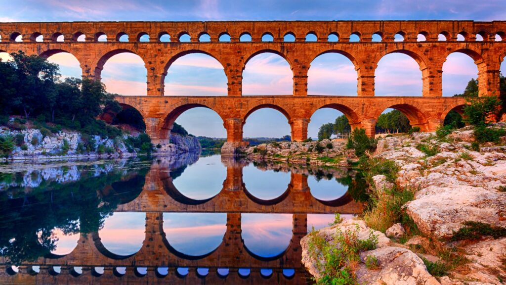 Pont du Gard se reflétant dans la rivière au coucher du soleil.